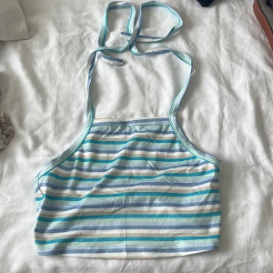 Randig linnetopp från SHEIN - Säljer en söt randig linnetopp från SHEIN i storlek S. Toppen har tunna axelband som knyts i nacken och är i mjuk polyester. Färgerna är ljusblå, turkos, beige och vit i horisontella ränder. Perfekt för varma dagar och en chill look.