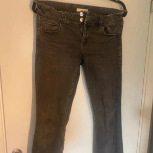 Grå bootcut jeans från Gina Tricot - Svarta jeans med bootcut-modell och två knappar i midjan. Klassisk femficksdesign och cool tvättad look. Jeansen har ett jättelitet hål i benet men det syns knappt och de är lite slitna längst ner. 