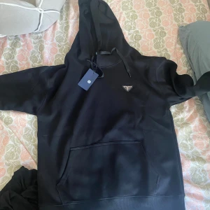 Prada hoddie  - Säljer en svart hoodie från Prada med klassisk huva och magficka. Tröjan har en liten metallogo på bröstet och ribbade muddar. Perfekt för en stilren och enkel look.