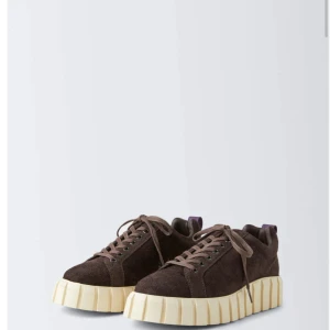Bruna sneakers från Eytys med platåsula - Säljer ett par bruna sneakers från Eytys med grov, beige platåsula och lila hälflik. Skorna har snörning och är tillverkade i mocka. Perfekta för dig som vill sticka ut med en chunky look.