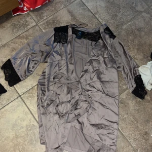 Siden morgon rock  - Snygg siden morgonrock från H&M i glansig polyester med svarta spetsdetaljer på axlar och ärmslut. Klänningen har lång ärm och knytband i midjan för en feminin siluett. Perfekt för dig som gillar en chic och elegant look.