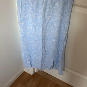 Ljusblå blommig lång kjol  - Säljer en ljusblå långkjol med vitt blommigt mönster. Kjolen har slits framtill och är tillverkad i ett lätt och luftigt material, perfekt för varma dagar. Dm för bilder med den på 