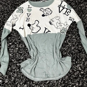 Grå och vit långärmad tröja med Disney-tryck - Har tvättarnas och pärlorna har inte gått av. Supper skön och kall för sommaren. Säljer en långärmad tröja i ljusgrått och vitt med tryck av Musse Piggs hand och texten LOVE. Dekorerad med pärlor på trycket. Perfekt för dig som gillar Disney och vill ha en unik topp.