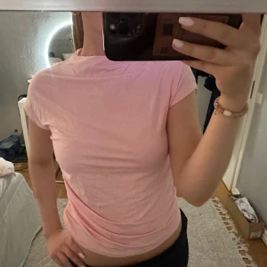 Ljusrosa t-shirt med rynkade sidor - Säljer en ljusrosa t-shirt med korta ärmar och rynkade detaljer längs sidorna. Toppen har en rund halsringning och är figurnära i passformen. Perfekt för en enkel och stilren look. Från lager157