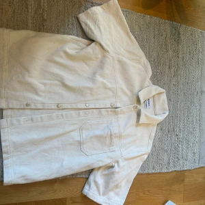 Vit kortärmad skjorta från Weekday - Säljer en stilren vit skjorta från Weekday med korta ärmar och klassisk krage. Skjortan har knäppning framtill och en bröstficka. Materialet är kraftigare och har en lätt struktur.