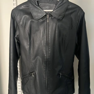Svart skinnjacka med dragkedja - Snygg svart skinnjacka från med dragkedja framtill och två fickor med dragkedja. Klassisk krage och figurnära passform. Perfekt för dig som vill ha en stilren och tidlös jacka i garderoben. 100% läder 