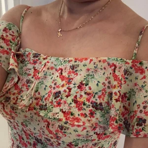 Ny Blommig sommarklänning från Zara - Supersöt blommig klänning från Zara Basic med tunna axelband och volangdetalj upptill. Klänningen har en ljus bas med färgglada blommor i rött, rosa och grönt. Perfekt för varma dagar och ger en fräsch vibe. Materialet känns lätt och luftigt.