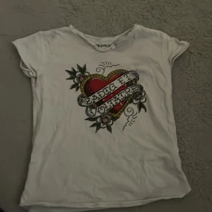 Vit t-shirt Zadig & Voltaire hjärttryck - Vit t-shirt från Zadig & Voltaire med coolt hjärttryck och banderoll på bröstet. Kortärmad modell i mjuk bomull, perfekt för en avslappnad och trendig look. Snygga detaljer med blommor och text på framsidan.