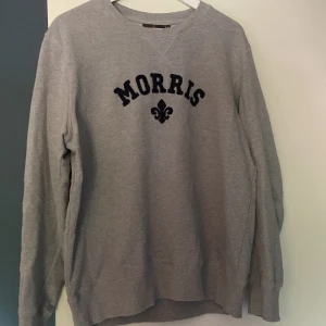 Morris tröja  - Snygg grå sweatshirt från Morris Stockholm med svart broderad logga och text på bröstet. Klassisk rund halsringning och långa ärmar. Perfekt för en chill och stilren look. Nypris: 1250kr