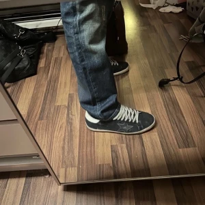 Mörkblå golden goose - Snygga svarta sneakers med vit sula och vita snören. Skorna har en tydlig stjärndetalj på sidan och texten 'GOLDEN GOOSE' tryckt bredvid. Perfekta för en avslappnad och trendig look. SÄLJ VÄLDIGT BILLIGT efter jag behöver pengar till resa så först till kvarn! Box medföljer