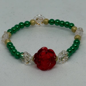 Armband med röd ros och gröna pärlor - 🌹 Armband – “Röd Ros” 🌹 Letar du efter något elegant, romantiskt och alldeles unikt?  Det här handgjorda armbandet är en hyllning till naturens färger och kärlekens symbol – rosen. Med skinande gröna pärlor, guldfärgade detaljer och vackra genomskinliga rosor, ramas allt in av en djup röd ros i centrum. Ett smycke som talar för sig själv!  ✨ Perfekt som present – till någon du tycker om, eller dig själv ✨ Trädd på elastisk tråd – passar de flesta handleder ✨ Endast ett exemplar!