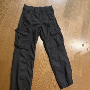 Svarta cargobyxor med fickor - Säljer ett par svarta cargobyxor med stretchig midja och vida ben. Aldrig använt.