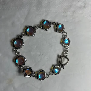 Handgjort armband  blåa glaskupoler - Handgjort armband av blåa glaskupoler som vackert ändrar färg i olicks ljus. Basen är av nickelfritt rostfritt stål, med ett sött stav lås iform av ett hjärta! Ett sv de hantverk som står mig varmt om hjärtat. Passar 17-18cm handled