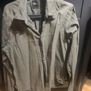 Olivgrön skjorta från Oscar Jacobson - Snygg olivgrön skjorta från Oscar Jacobson i slim fit-modell. Skjortan har klassisk krage, långa ärmar och knäppning framtill. Perfekt för dig som gillar stilrena och enkla plagg med en modern passform. Storleken är L men sitter som en M eftersom den har krympt när den har blivit tvättad.