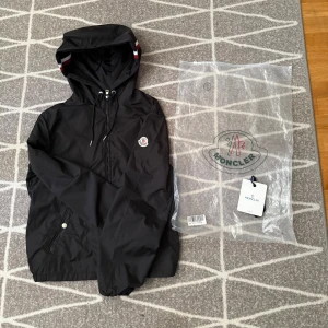 Moncler windbreaker Svart - Svart windbreaker (vindjacka) från Moncler med huva i Storlek 2 (M) i helt ny skick. Påse samt etiketter tillkommer, vid intresse hör av er, pris kan även diskuteras