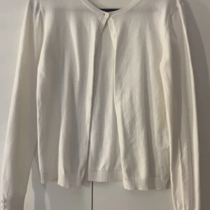 Vit kofta med knappar - En klassisk vit kofta med rund halsringning och knäppning framtill. Långa ärmar med ribbade muddar och enkla knappar vid halsen och ärmsluten. Perfekt att slänga över en topp för en clean och stilren look.