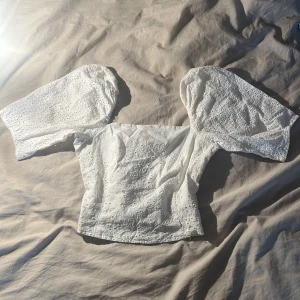 Vit broderad blus med puffärm - Superfin vit blus med broderade detaljer och stora puffärmar. Toppen har vackert hålmönster och dragkedja i sidan för enkel påklädning. Perfekt för dig som gillar romantisk och trendig stil med extra volym på ärmarna💗 säljer för att jag använder den inte något mer💗☀️