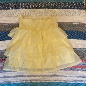 Gul volangkjol med resårmidja - Söt ljusgul kortkjol med flera lager volanger och bred resår i midjan. Från vero Moda 