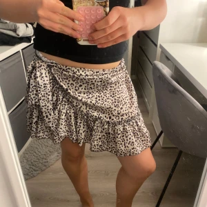Leopardmönstrad omlottkjol med volang - Superfin kort omlottkjol med leopardmönster i beige och svart. Kjolen har volangkant och knyts i sidan för en snygg passform. Stl l men sitter som en m/s