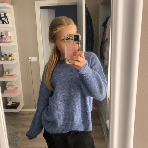 Blå stickad tröja med loose fit - Mysig blå stickad tröja med rund halsringning och ribbade muddar. Modellen är loose fit och har långa ärmar. Perfekt för lager-på-lager och chill dagar. Färgen är en mjuk blå ton som passar till det mesta.