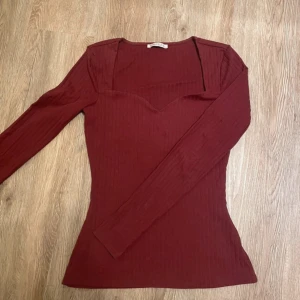 Vinröd ribbad långärmad topp - Säljer en vinröd långärmad topp med ribbad struktur och snygg v-ringning. Toppen har en figurnära passform och är perfekt att styla till olika outfits. Superfin färg och enkel att matcha!