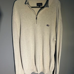 Beige stickad tröja med half-zip från Lexington - Säljer en beige stickad tröja från Lexington med halv dragkedja och liten logotyp på bröstet. Tröjan har lång ärm och ribbade muddar. Perfekt för lager-på-lager och stilren vardagslook. Passar både M och L