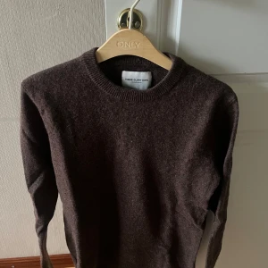Mörkbrun stickad tröja These Glory Days - Mysig mörkbrun stickad tröja från These Glory Days. Klassisk rund halsringning och långa ärmar. Perfekt för lager-på-lager och passar till både jeans och chinos. Enkel och stilren design som funkar året runt.