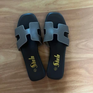 Bruna sandaler  - Säljer ett par bruna sandaler med öppen fyrkantig tå och breda remmar i syntetmaterial. Perfekta för varma dagar och enkla att matcha till olika outfits. Stolek 37-38, helt oanvända 