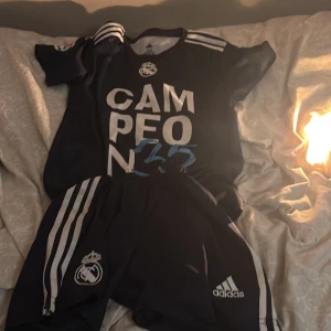 Svart fotbollströja från Adidas -  PRIS kan diskuteras! Va inte rädd och ställa frågor🙂 , Snygg svart fotbollströja från Adidas med texten 'CAMPEON 35' och Real Madrids emblem. Tröjan har korta ärmar och tre vita ränder på axlarna. Perfekt för fans av Real Madrid!