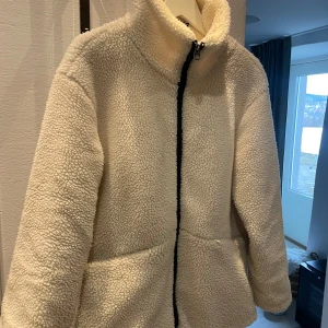 Vit teddyjacka från Vero Moda - Oversized vit teddyjacka från Vero Moda med dragkedja framtill. Jackan har en hög krage och två praktiska fickor. Stl XS men sitter rent storleksmässigt som kanske M. Går nedanför rumpan på mig som är 172. Det är lite smink rester på kragen, ska ta bort det som går. 