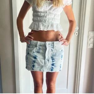 Blåvit jeanskjol - Snygg kort jeanskjol i blått och vitt med ett unikt mönster. Kjolen har en klassisk femficksdesign och knappar framtill. Perfekt för en avslappnad stil.