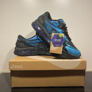 Svart och blåa sneakers från Asics - Säljer ett par snygga Asics sneakers i svart och blått. Skorna har en sportig design med snörning och en bekväm sula. Perfekta för träning eller en aktiv vardag.