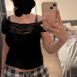 Svart topp med spetsdetaljer - Säljer en elegant svart topp med spetsdetaljer över axlarna och bröstet. Toppen har en offshoulder-design och är perfekt för en stilren look. Passar bra till både jeans och kjol.