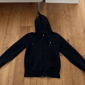 Svart hoodie från Polo Ralph Lauren - Säljer en mörkblå polo Ralph lauren hoodie. De är en mycket snygg och stilren tröja. Funkar både till lite festligare och vardagligt andvänd. Den kostar ny 2000+kr. Hör av er vid minsta fråga.