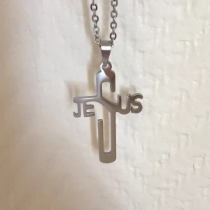 Silverfärgat korshalsband - Snyggt silverfärgat halsband med ett korsformat hänge där ordet 'Jesus' är integrerat i designen. Perfekt för att uttrycka din tro med stil. Kedjan är av metall och har en klassisk länkdesign.