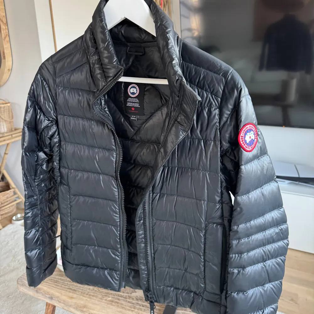 Säljer en snygg svart dunjacka från Canada Goose. Jackan har en klassisk design med dragkedja och är perfekt för kyligare väder. Den är lätt och smidig att bära, med en stilren look som passar till det mesta. Perfekt för dig som vill hålla värmen med stil! 🖤. Takit.