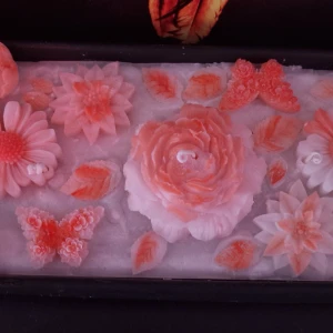 Dekorativa ljus i form av blommor och fjärilar - Vackra dekorativa ljus i form av blommor och fjärilar i en mjuk rosa nyans. Perfekt för att skapa en mysig atmosfär i hemmet. Ljusen är placerade i en rektangulär behållare och har detaljerade mönster som liknar kronblad och vingar.