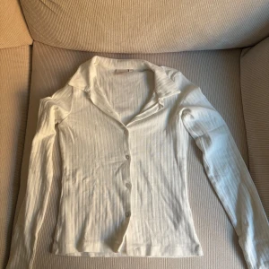 Vit ribbad tröja - Säljer en stilren vit ribbad tröja/kofta från Nelly. Den har långa ärmar och knappar framtill. Endast använd en gång!