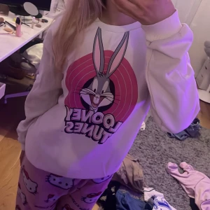 Vit Looney Tunes tröja från H&M - Säljer en vit tröja från H&M med ett stort Looney Tunes-tryck på framsidan. Tröjan har långa ärmar och en rund halsringning. Perfekt för alla som älskar klassiska tecknade serier!