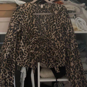 Leopardmönstrad blus med knytning - Säljer en leopardmönstrad blus med knytning framtill. Blusen har långa ärmar och en v-ringad design.