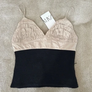 Beige och svart topp från Zara - Snygg topp från Zara med beige överdel och svart underdel. Den har smala axelband och en rynkad detalj på bysten. Perfekt för en stilren look. Aldrig använd och prislappen kvar då han ej returnera ❤️