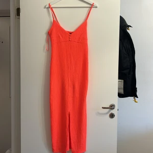 Orange klänning från Gina Tricot - Snygg orange klänning från Gina Tricot med smala axelband och en stilren slits framtill. Perfekt för en somrig look. Klänningen har en texturerad yta som ger den en unik touch.