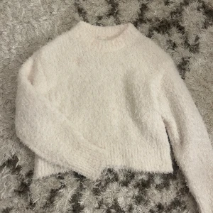 Vit fluffig tröja - Mysig vit fluffig tröja med lång ärm och rund hals. Perfekt för kyliga dagar när du vill känna dig varm och bekväm. Tröjan har en enkel design som gör den lätt att matcha med olika outfits.