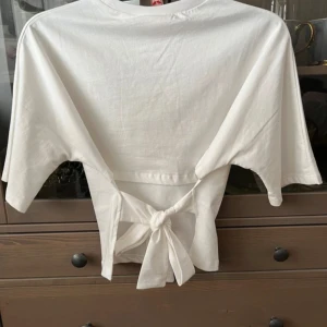 Vit topp från Nelly - Säljer en stilren vit topp från Nelly med knytning i ryggen. Toppen har korta ärmar och en rund halsringning. Perfekt för en avslappnad look. Använt fåtals gånger, normal i storleken, pris kan diskuteras 💞