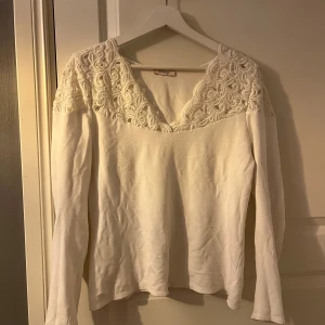 Vit långärmad topp från Orsay - Säljer en elegant vit långärmad topp från Orsay med vackra spetsdetaljer vid axlarna och en v-ringad design. Perfekt för en stilren look. Passar bra till både jeans och kjol.
