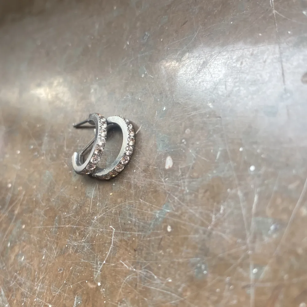 Säljer ett par eleganta silverfärgade örhängen i creolmodell. De är dekorerade med gnistrande stenar längs framsidan som ger en lyxig känsla. Perfekta för att ge en extra touch till din outfit.. Asusteet.