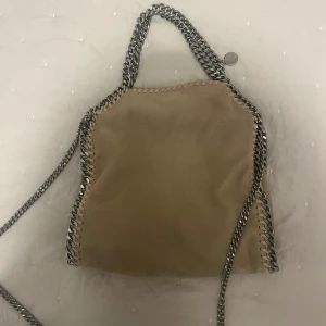  Stella McCartney väska - Väska från Stella Mccartney i modellen Falabella. Handväska med axelrem. Äkthetsbevis medkommer och syns även på bild (lappen i väskan och orginal lapp vis köp). Lite fläckig på insidan men annars i väldigt bra skick, inga defekter på utsidan väskan. Tar gärna emot bud! Kontakta gärna innan köp.