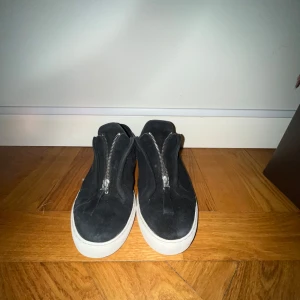 Axel Arigato skor - Snygga svarta sneakers från Axel Arigato i mocka med dragkedja framtill. Skorna har en vit sula som ger en stilren kontrast. Perfekta för en trendig look. Skorna är i använt skick men inget som påbörjar skorna. Nypris: 2800kr, mitt pris: 699kr