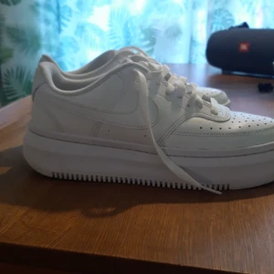 Vita sneakers från Nike - Snygga vita sneakers från Nike med klassisk design och snörning. Skorna har en tjock sula och är perfekta för en stilren look. Perfekta för dig som vill ha en tidlös stil.