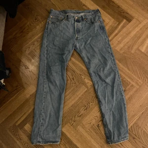 Blå jeansbyxor  Levis 501 - Klassiska blå jeansbyxor med fem fickor och knappgylf Levis 501. De har en rak passform och är tillverkade i slitstarkt denimtyg. Perfekta för en avslappnad stil.